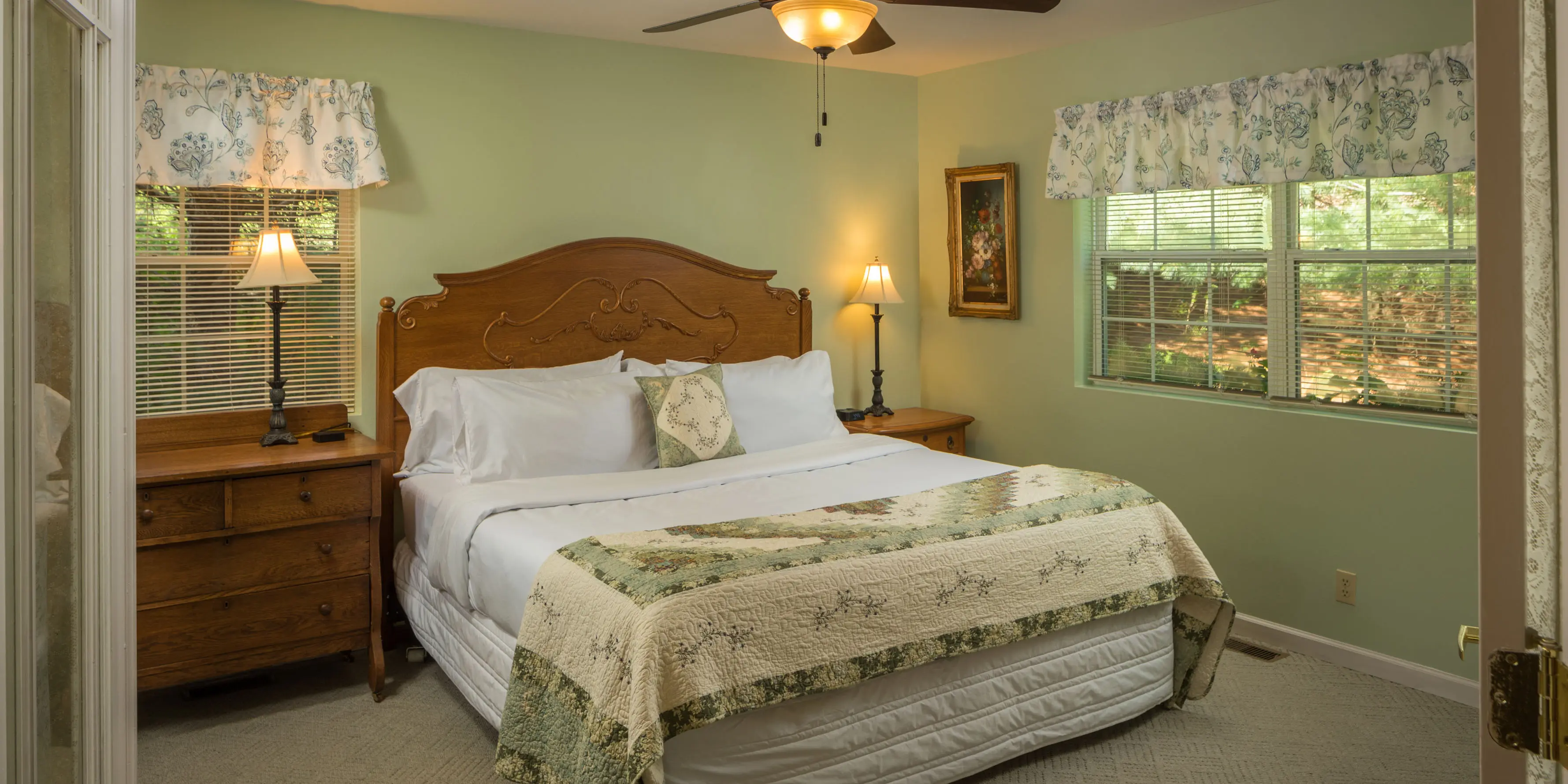 light green room with large white bed with dresser and nightstand