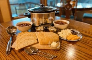 pot of chili , loaf of bread and cheese plate