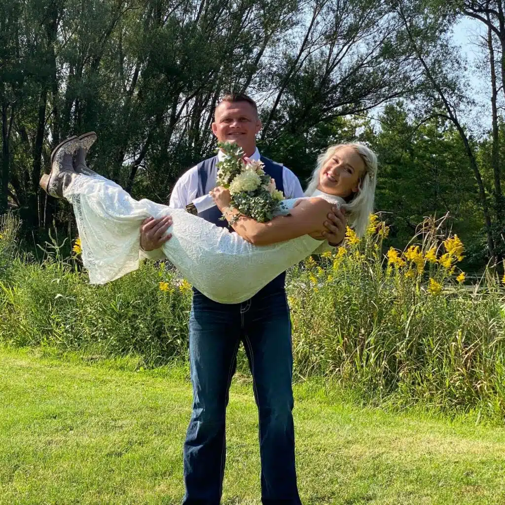 Groom carrying bride in front of pond during thier intimate wedding