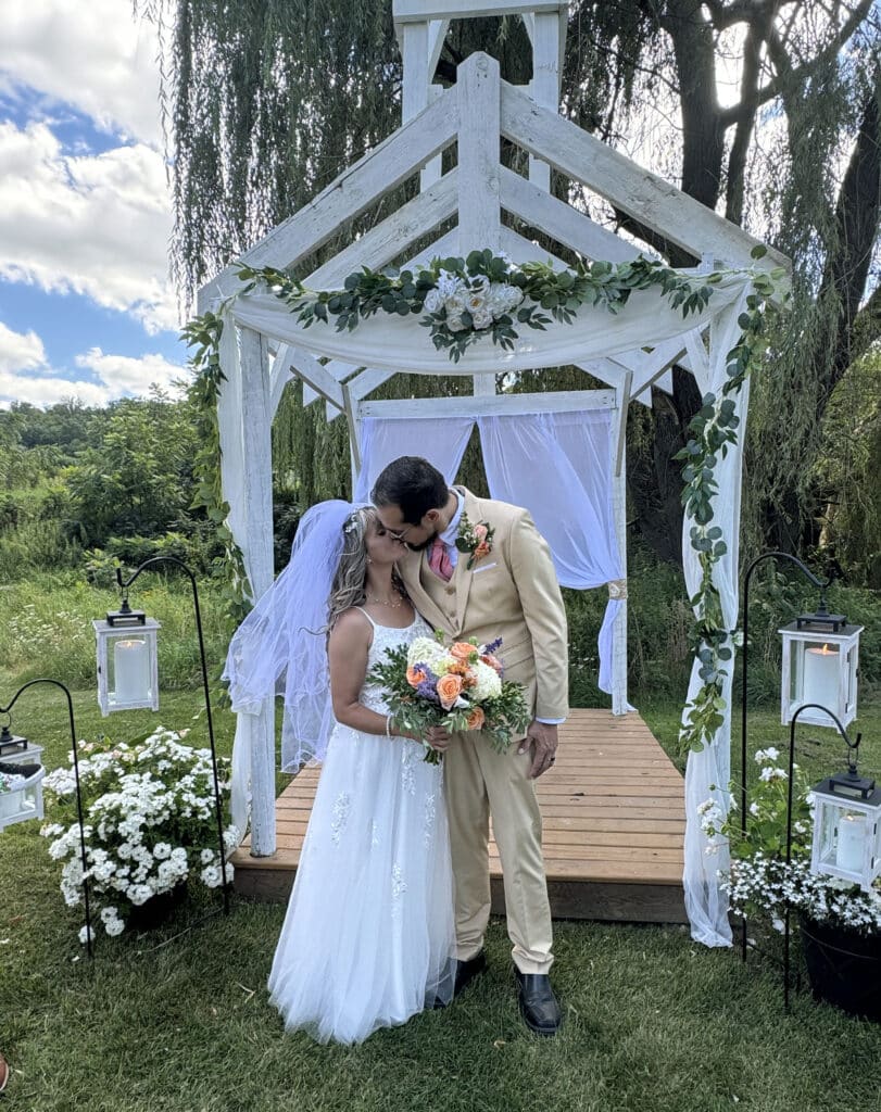 Wedding couple kissing under rustic wedding arbor