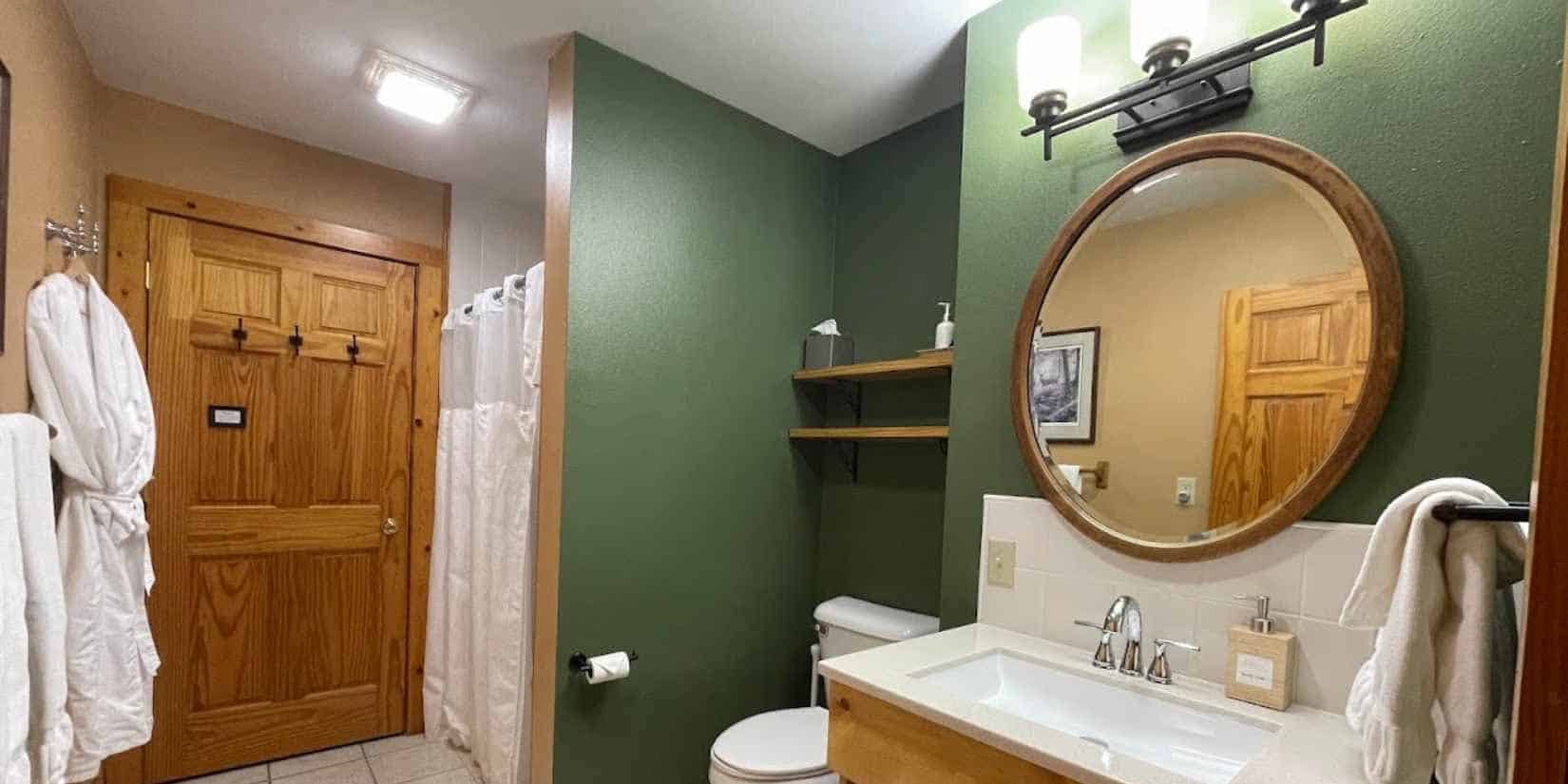 Bathroom with sink, toilet, and shower. Green walls and white linens