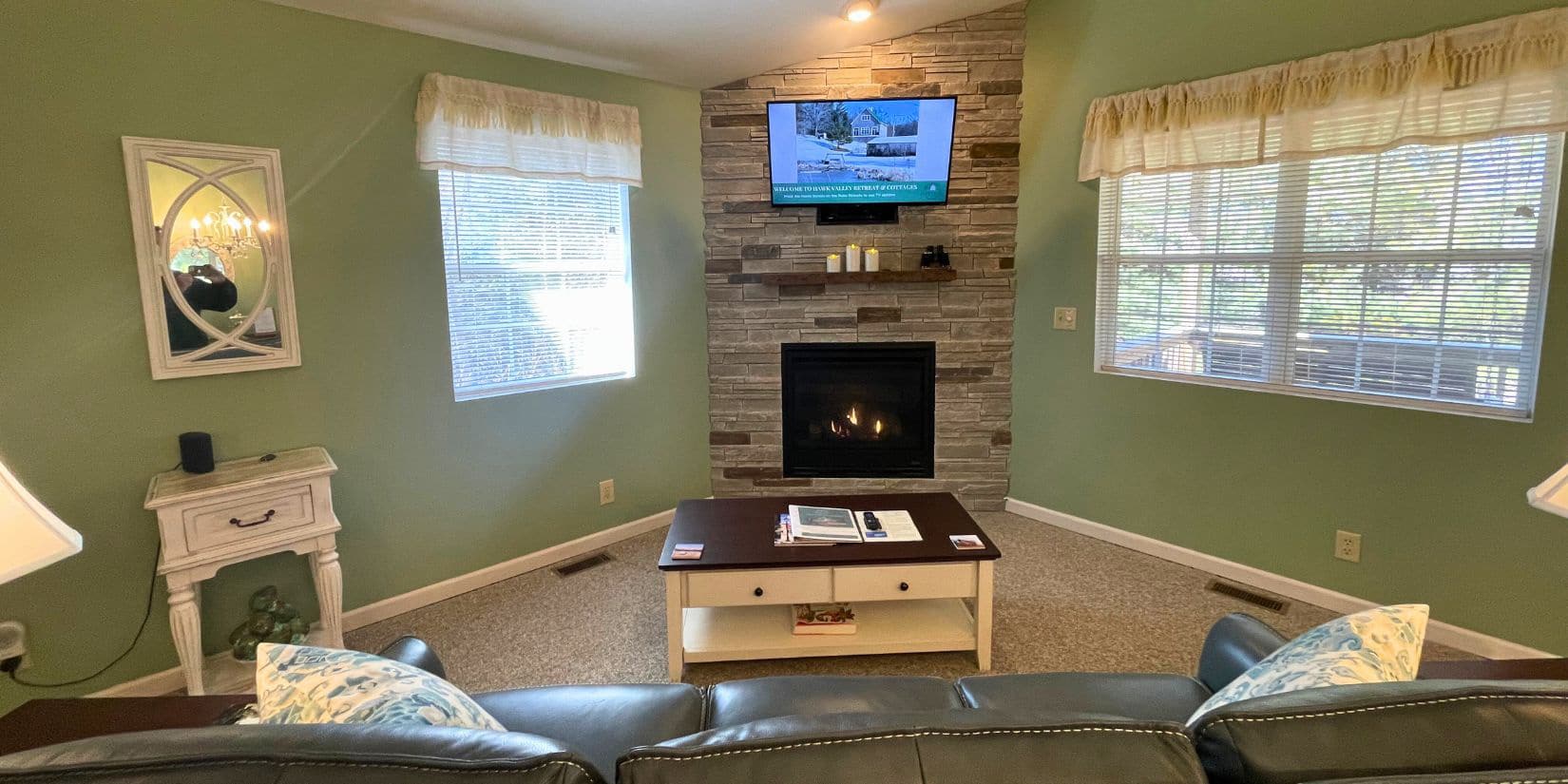 Green room with tv over fireplace, couch and tables.