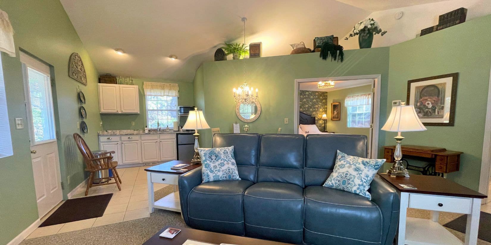 grey reclining couch in green room with white kitchen in background