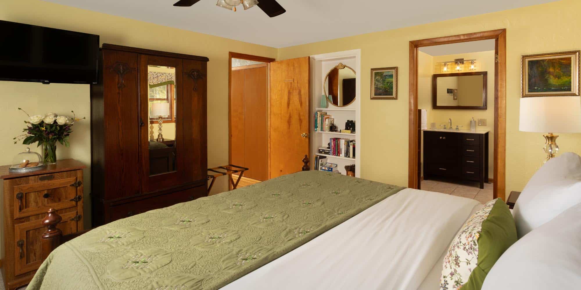 large bed with armoir, tv, and bathroom in backround