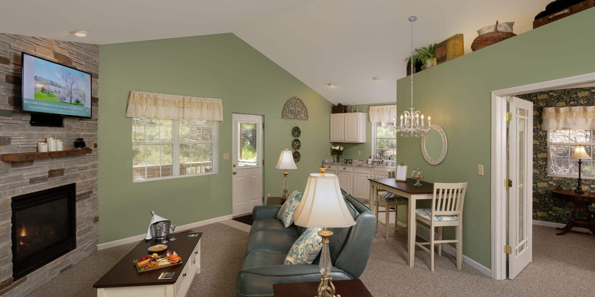 green walls with stone fireplace and couch looking into kitchen and bedroom