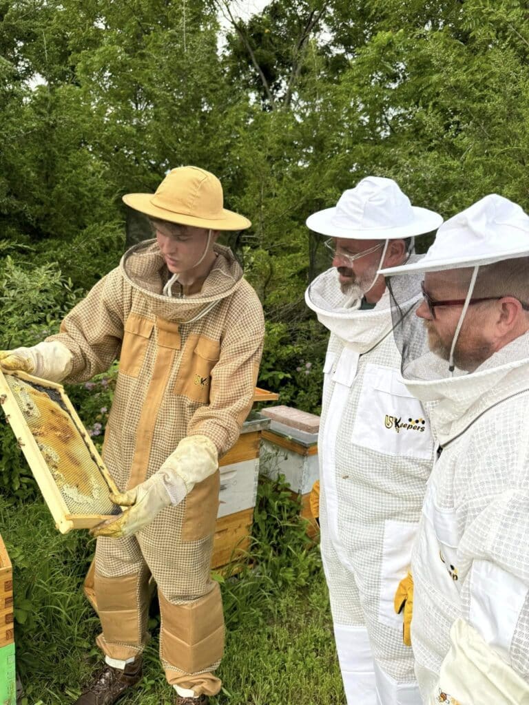 dry creek beekeeper showing two men a frame of bees